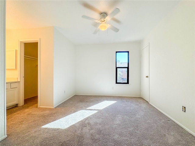 unfurnished bedroom featuring ceiling fan, light carpet, a closet, and a walk in closet