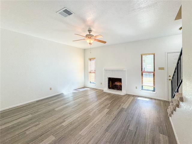 unfurnished living room with a fireplace, wood-type flooring, a textured ceiling, and ceiling fan