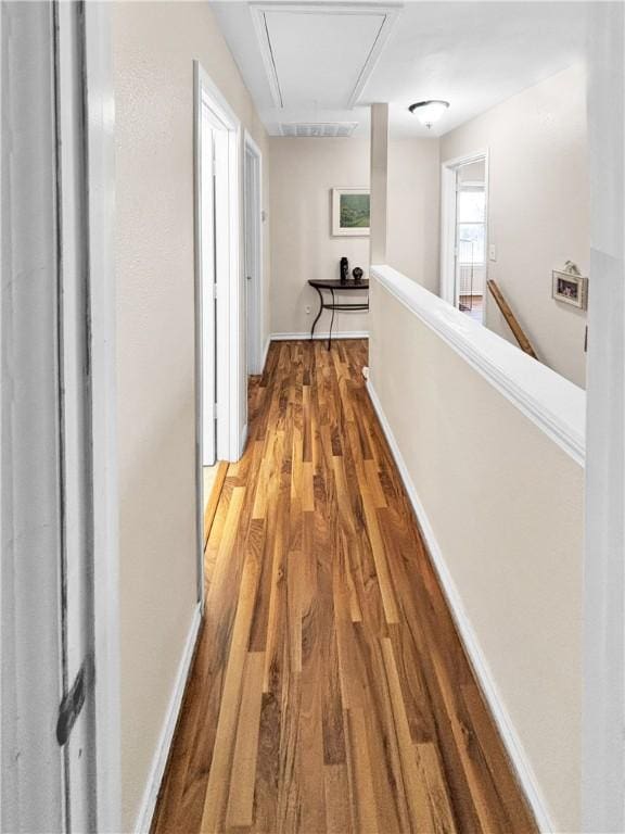 hallway with an upstairs landing, attic access, baseboards, and wood finished floors