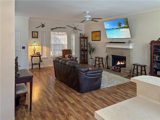 living room with a brick fireplace, baseboards, ceiling fan, ornamental molding, and wood finished floors