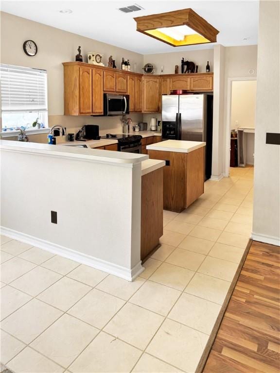 kitchen featuring a center island, light countertops, brown cabinets, appliances with stainless steel finishes, and a peninsula