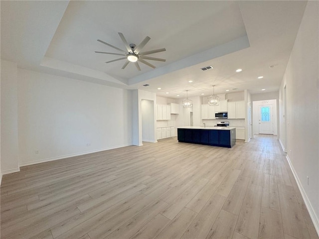 unfurnished living room with ceiling fan with notable chandelier, light wood-type flooring, a raised ceiling, and sink