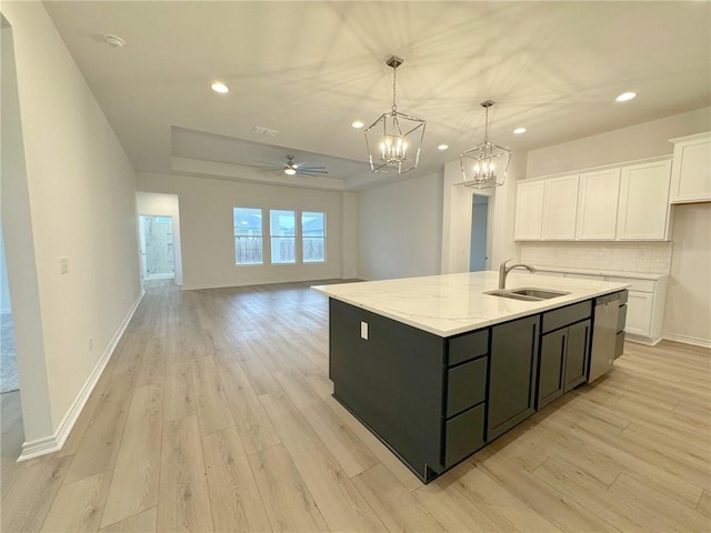 kitchen with a center island with sink, ceiling fan with notable chandelier, hanging light fixtures, light hardwood / wood-style floors, and white cabinetry