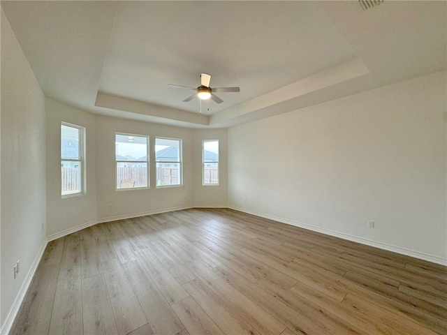 empty room featuring light hardwood / wood-style floors, ceiling fan, and a tray ceiling