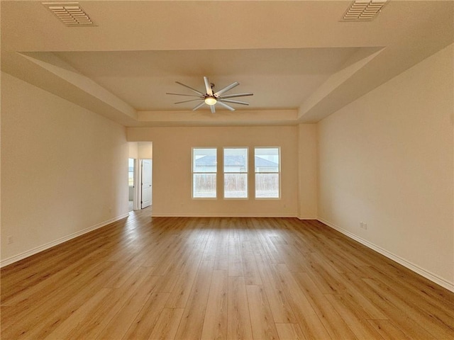 empty room with a raised ceiling, light hardwood / wood-style flooring, and ceiling fan