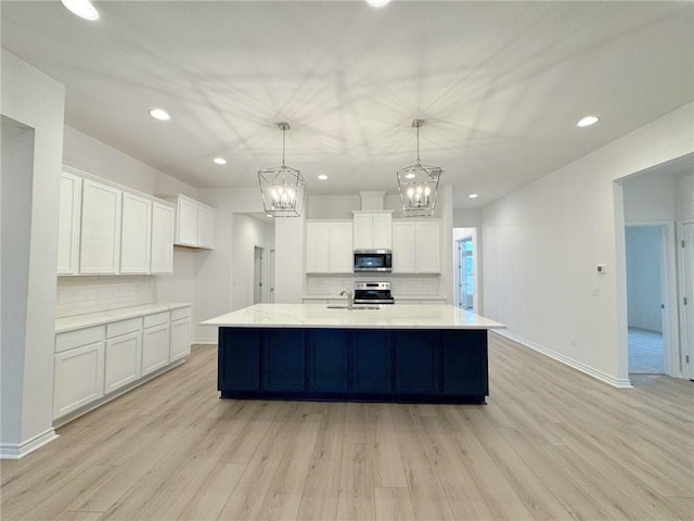 kitchen featuring pendant lighting, white cabinetry, appliances with stainless steel finishes, and light hardwood / wood-style flooring