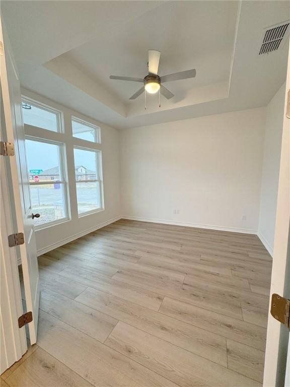 spare room featuring ceiling fan, a raised ceiling, and light wood-type flooring