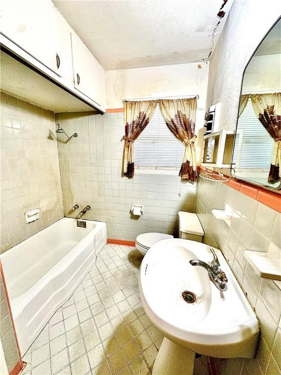 full bathroom with a textured ceiling, toilet, tile walls, and tiled shower / bath combo