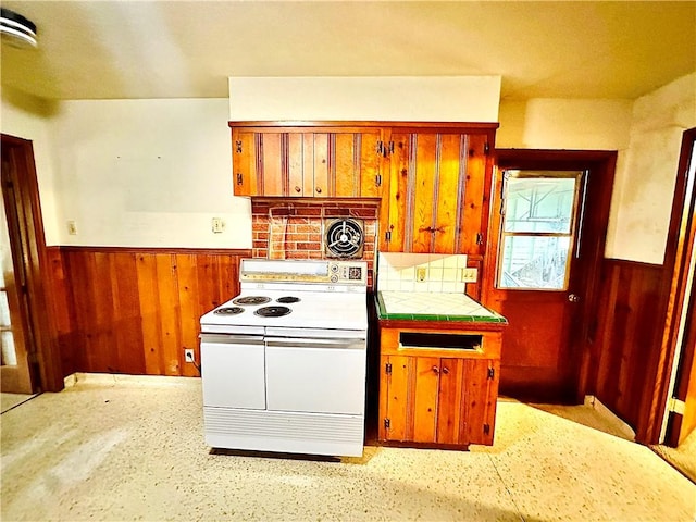 kitchen with tasteful backsplash, electric range, tile counters, and wood walls