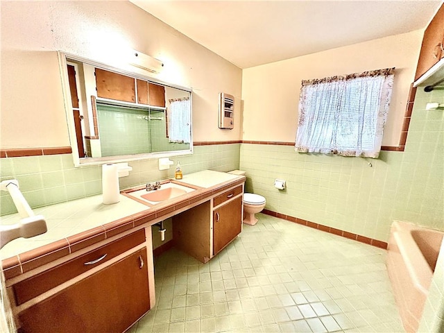 bathroom with a washtub, vanity, toilet, and tile walls