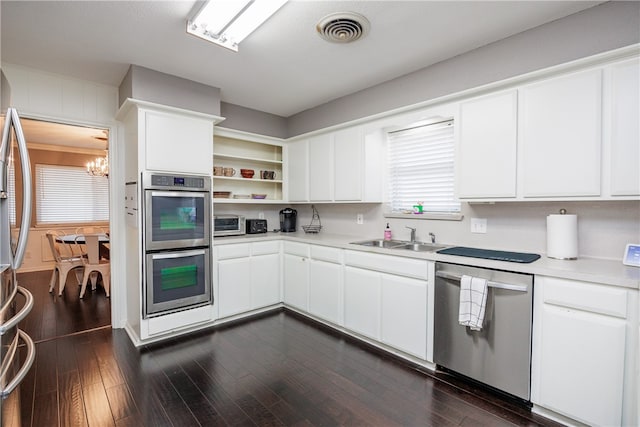 kitchen with sink, dark wood-type flooring, stainless steel appliances, a chandelier, and white cabinets