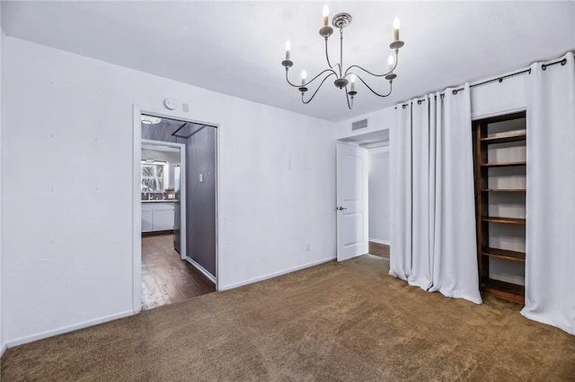 unfurnished bedroom featuring a notable chandelier, dark carpet, and ensuite bath