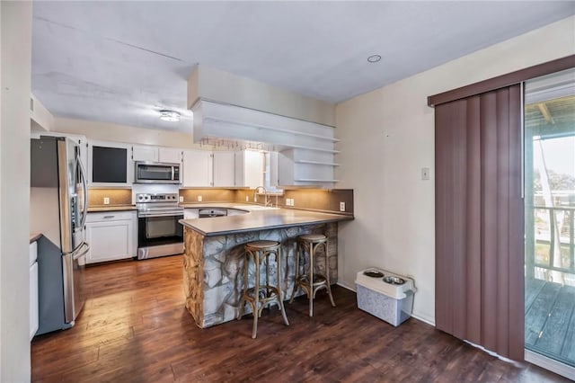 kitchen featuring appliances with stainless steel finishes, white cabinetry, sink, a kitchen breakfast bar, and kitchen peninsula