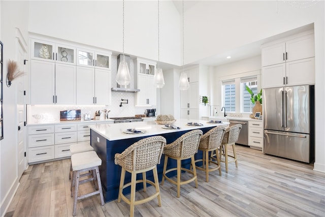 kitchen with white cabinets, a high ceiling, stainless steel appliances, and wall chimney exhaust hood