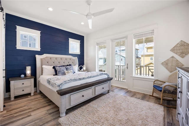 bedroom featuring access to outside, ceiling fan, wooden walls, and dark hardwood / wood-style floors