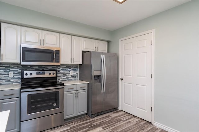 kitchen featuring wood-type flooring, gray cabinets, decorative backsplash, white cabinets, and appliances with stainless steel finishes