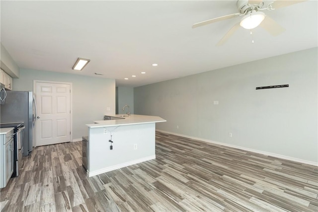 kitchen with ceiling fan, sink, stainless steel appliances, light hardwood / wood-style floors, and a kitchen island with sink