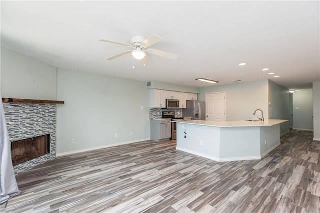 kitchen featuring a stone fireplace, sink, ceiling fan, white cabinetry, and stainless steel appliances