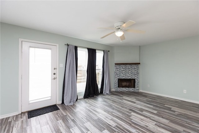 unfurnished living room featuring hardwood / wood-style flooring, ceiling fan, a healthy amount of sunlight, and a stone fireplace