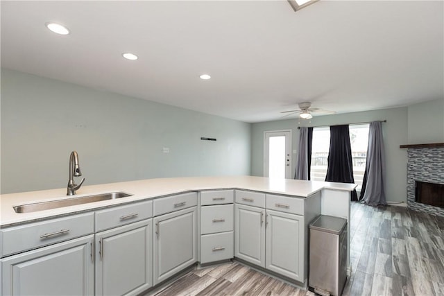 kitchen featuring kitchen peninsula, ceiling fan, sink, light hardwood / wood-style floors, and a stone fireplace