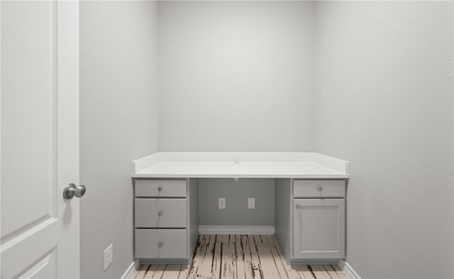 office space with light wood-style flooring, built in desk, and baseboards