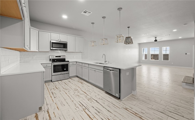 kitchen featuring pendant lighting, stainless steel appliances, light countertops, open floor plan, and a sink