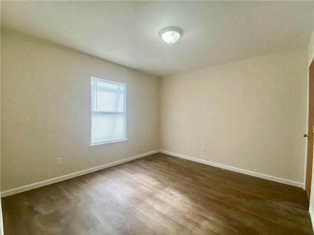 spare room featuring dark wood-style flooring and baseboards