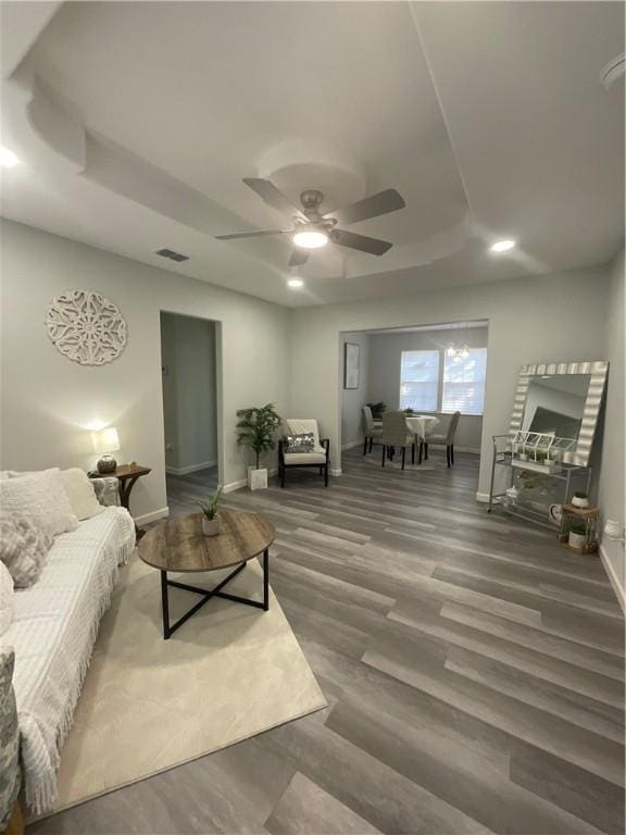 living area featuring baseboards, visible vents, a raised ceiling, ceiling fan, and wood finished floors