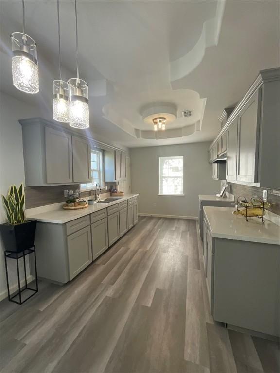 kitchen with gray cabinets, a raised ceiling, light countertops, light wood-style floors, and a sink