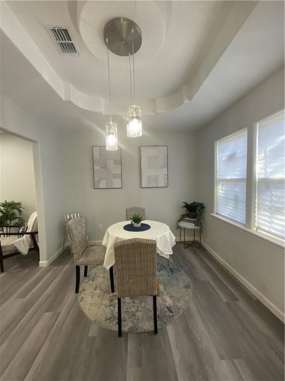 dining space featuring baseboards, visible vents, a tray ceiling, and wood finished floors