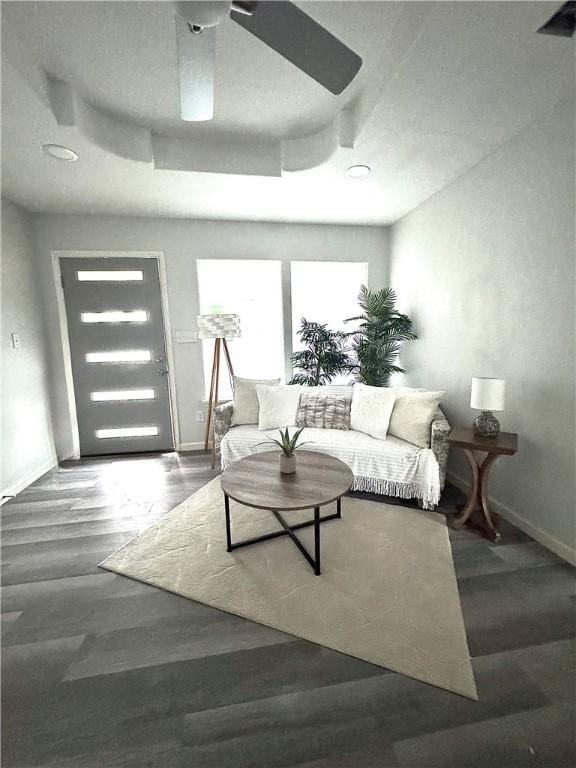 living room with a raised ceiling, ceiling fan, and dark hardwood / wood-style flooring