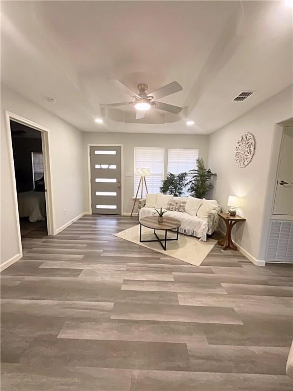 living area featuring a ceiling fan, visible vents, baseboards, and wood finished floors