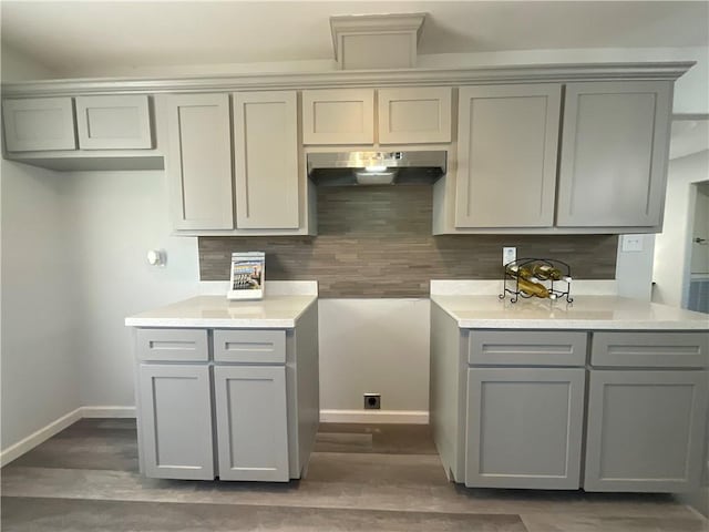 kitchen featuring tasteful backsplash, baseboards, under cabinet range hood, and gray cabinetry