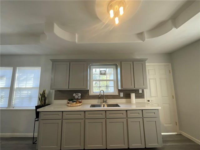 kitchen featuring a sink, baseboards, a raised ceiling, and gray cabinetry