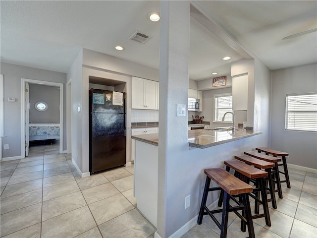 kitchen featuring stone counters, white cabinets, black refrigerator, sink, and kitchen peninsula