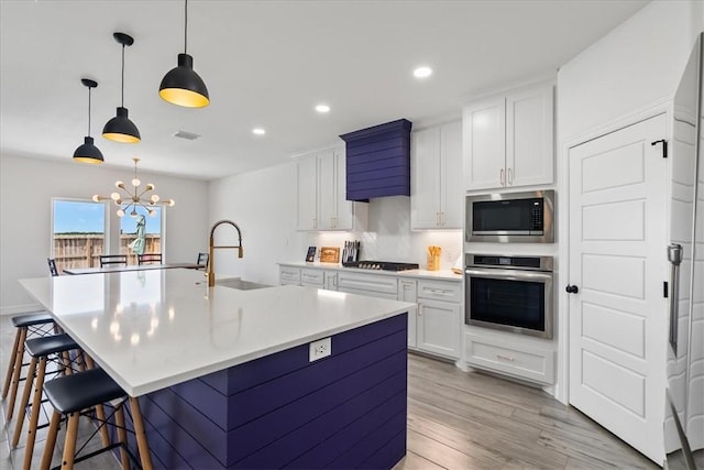 7910 Parham Dr, Corpus Christi, TX 78414 - kitchen featuring stainless steel appliances, light wood-type flooring, white cabinets, an island with sink, and a breakfast bar