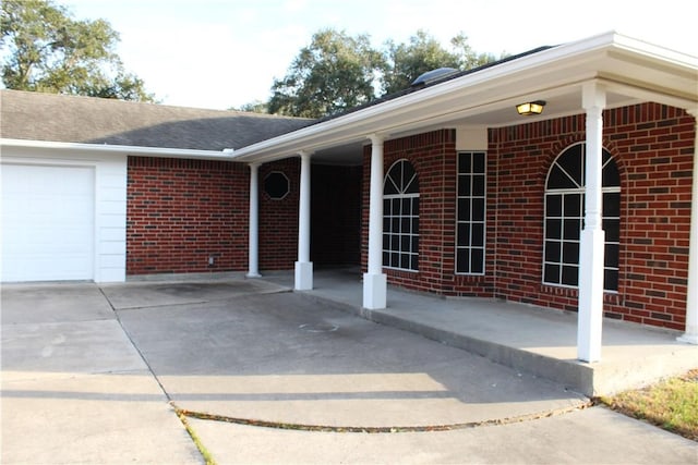 exterior space featuring an attached garage, roof with shingles, concrete driveway, and brick siding