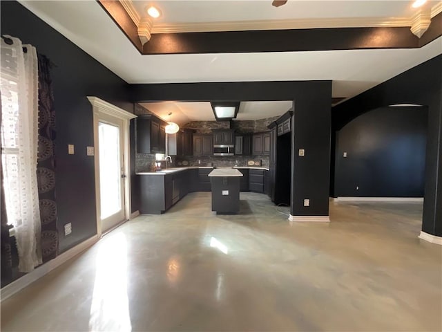 kitchen with a sink, stainless steel microwave, tasteful backsplash, a center island, and baseboards