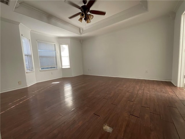 spare room with baseboards, ceiling fan, a tray ceiling, ornamental molding, and dark wood-style flooring