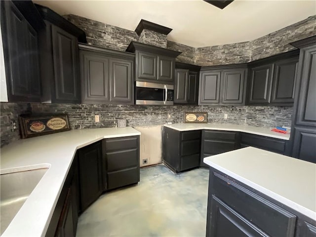 kitchen featuring stainless steel microwave, backsplash, light countertops, concrete flooring, and a sink