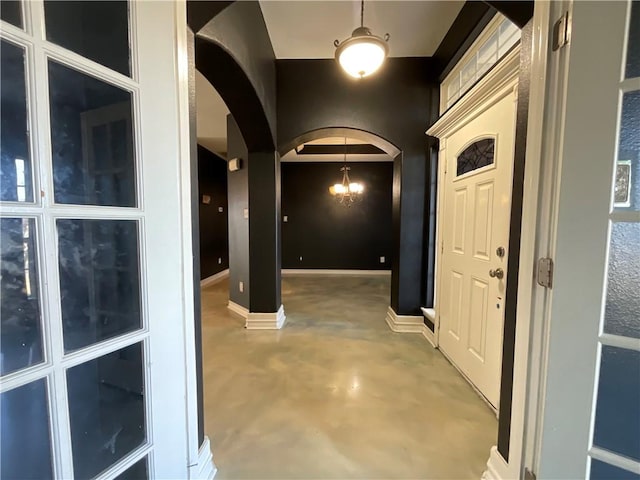 foyer with a notable chandelier, baseboards, arched walkways, and concrete floors