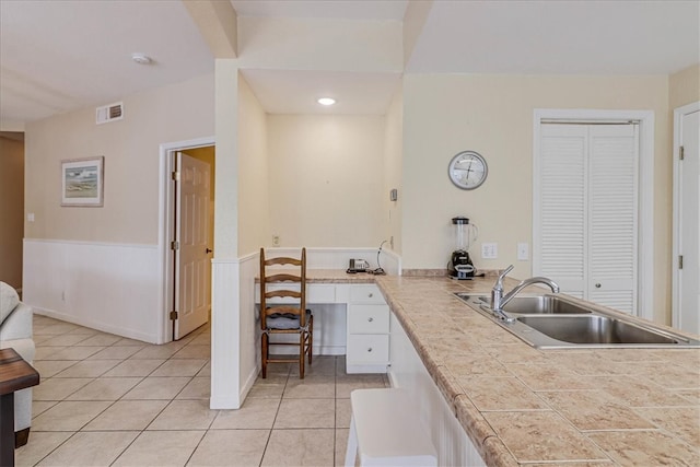 kitchen featuring built in desk, sink, light tile patterned floors, and white cabinets