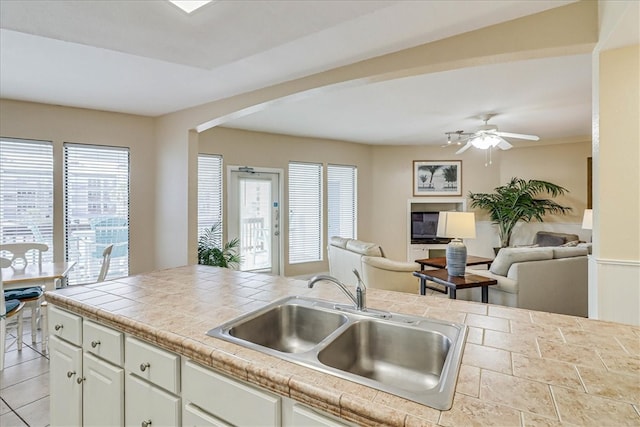 kitchen with tile counters, ceiling fan, white cabinetry, and sink