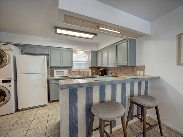 kitchen with kitchen peninsula, a breakfast bar area, white appliances, stacked washer / dryer, and decorative backsplash