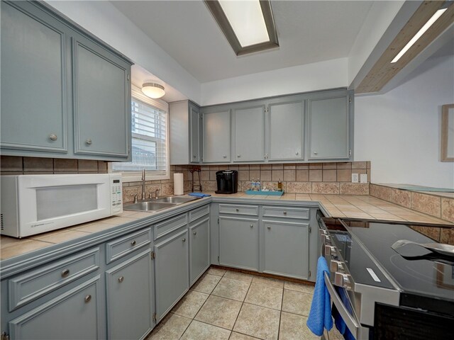 kitchen featuring tile counters, gray cabinets, sink, and backsplash