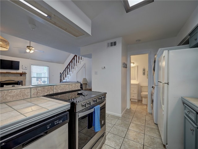 kitchen featuring stainless steel appliances, light tile patterned floors, tile countertops, lofted ceiling, and ceiling fan