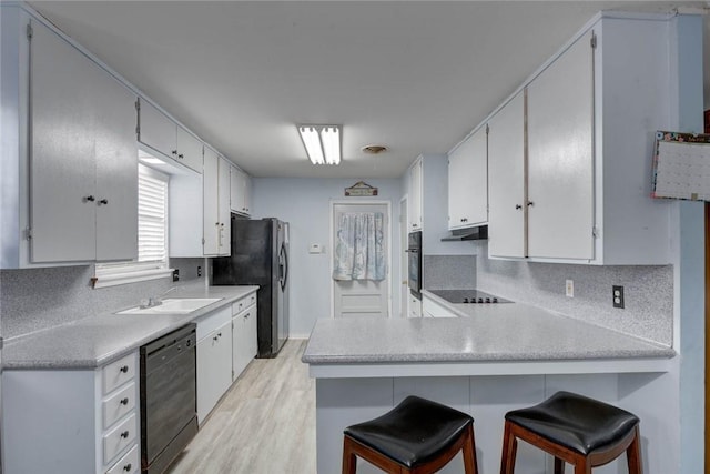 1038 Herndon St, Corpus Christi, TX 78411 - kitchen with black appliances, a peninsula, backsplash, under cabinet range hood, and light wood-style floors