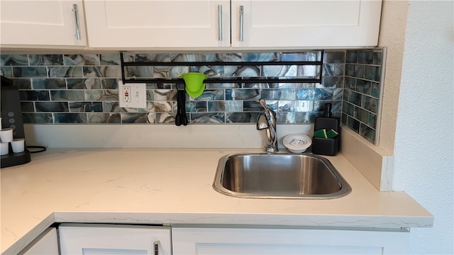 interior details with white cabinetry, sink, and light stone countertops