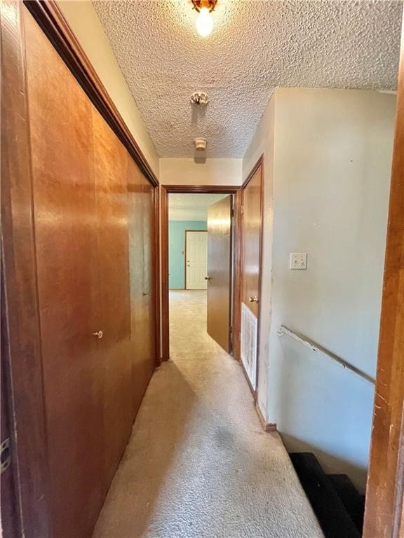 hallway with light colored carpet and a textured ceiling