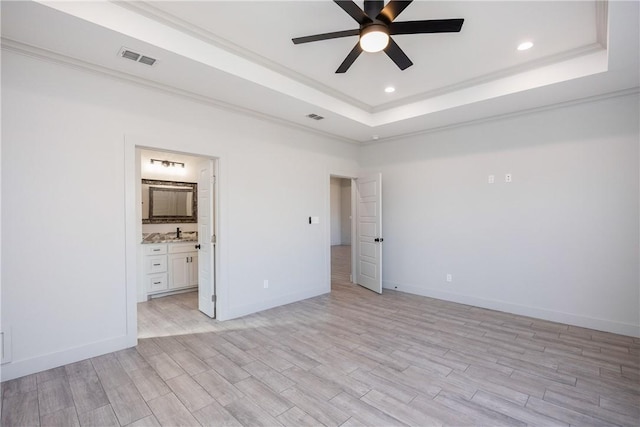 unfurnished bedroom with ensuite bath, ceiling fan, a raised ceiling, light hardwood / wood-style floors, and ornamental molding